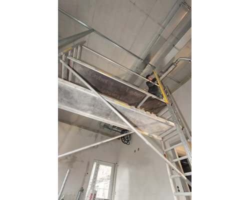 Vakman op een Layher rolsteiger tijdens installatiewerkzaamheden aan een betonnen plafond in een ruwbouw.