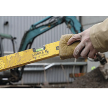 Stabila waterpas type 70 wordt schoongemaakt met een spons, hand houdt de vuile gele waterpas vast op een bouwplaats.