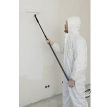 Man in wit beschermend pak en veiligheidsbril verft een muur met een verfroller aan een telescoopsteel.