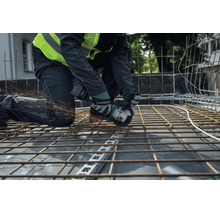Een bouwvakker snijdt met een Metabo accu haakse slijper door een stalen wapeningsnet op een bouwplaats.
