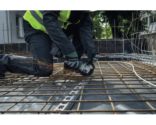Een bouwvakker snijdt met een Metabo accu haakse slijper door een stalen wapeningsnet op een bouwplaats.