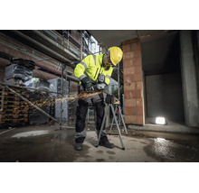 Bouwvakker in reflecterende kleding en veiligheidshelm gebruikt een Metabo haakse slijper op een werkstuk op een bouwplaats met rondvliegende vonken.