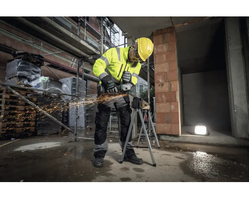 Bouwvakker in reflecterende kleding en veiligheidshelm gebruikt een Metabo haakse slijper op een werkstuk op een bouwplaats met rondvliegende vonken.