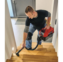 Een man reinigt een houten trap met een compacte Einhell accu nat-droogzuiger.
