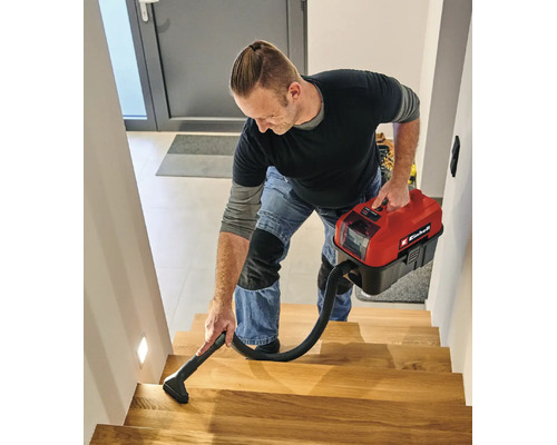 Een man reinigt een houten trap met een compacte Einhell accu nat-droogzuiger.