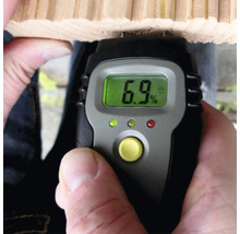 Digitale vochtmeter meet het vochtgehalte van een houten plank, het display geeft zes komma negen procent aan.