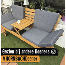 Houten tuinbank met grijze kussens en geïntegreerde uitklapbare bijzettafel op kunstgras, Instagram Logo.