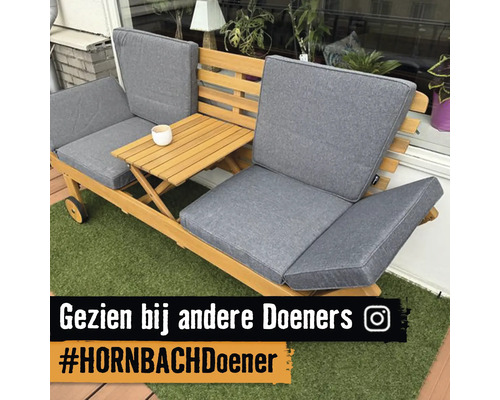 Houten tuinbank met grijze kussens en geïntegreerde uitklapbare bijzettafel op kunstgras, Instagram Logo.