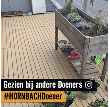 Georganiseerd balkon met terrasplanken en een houten moestuinbak op poten met bloemen en tuingereedschap op de plank.