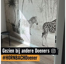 Wand met safari-behang met een zebra, giraffe en palmbomen in een lichte kamer met houten vloer en een krukje.
