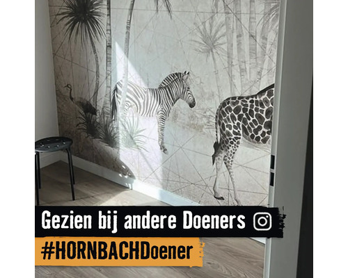 Wand met safari-behang met een zebra, giraffe en palmbomen in een lichte kamer met houten vloer en een krukje.