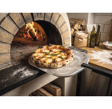 Versgebakken pizza op een pizzaschep met Tenneker Logo voor een brandende steenoven in een rustieke keuken.