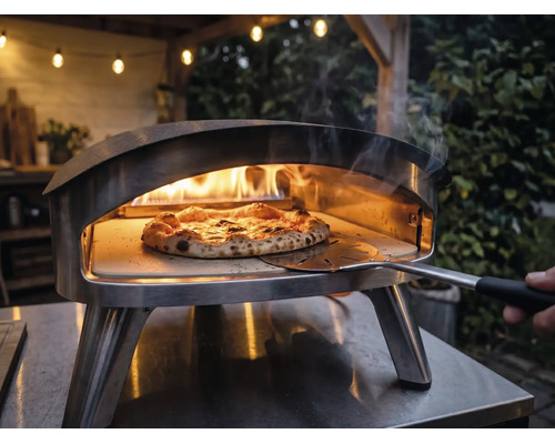 Roestvrijstalen pizzaoven voor buiten met brandende vlammen en een pizza op een pizzasteen die met een pizzaschep wordt verplaatst.