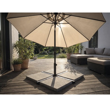 Parasol op een houten terras met parasolvoet van betonplaten, tuinmeubelen en planten in een lichte buitenruimte.