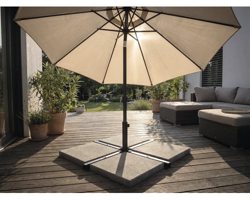 Parasol op een houten terras met parasolvoet van betonplaten, tuinmeubelen en planten in een lichte buitenruimte.