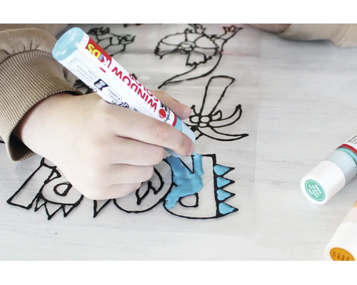 Hand van een kind die een dinosaurusmotief op een transparante folie inkleurt met Marabu Window Color Kids.