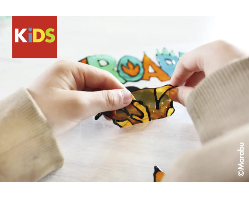 Kinderhanden maken een raamverfsticker met dinosauruspatroon los. Marabu Logo en KIDS Logo.