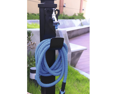 Zwarte tuinwatertap met zilverkleurige kraan en een opgerolde blauwe tuinslang aan een houder in de buitenlucht.