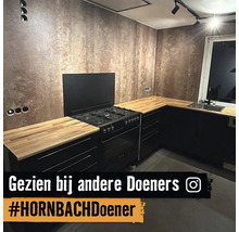 Moderne keuken met zwarte kasten, een houten werkblad, een gasfornuis en een muur met een bronzen textuurafwerking.