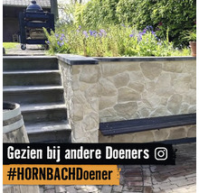 Tuininrichting met een natuurstenen muur, een geïntegreerde houten bank en stenen trappen naast een bloemborder.