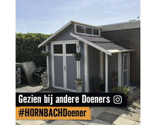 Grijs houten tuinhuis met witte details, dubbele deuren met ramen, zadeldak en aanbouw met afdak in een tuin.