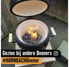 Kamado keramische barbecue met open deksel en brandende houtskool op een houten tafel. Instagram Logo. Gezien bij andere Doeners. HORNBACH Doener.