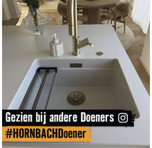 Moderne witte onderbouw spoelbak met gouden kraan, zeepdispenser en afdruiprek in een lichte keuken.