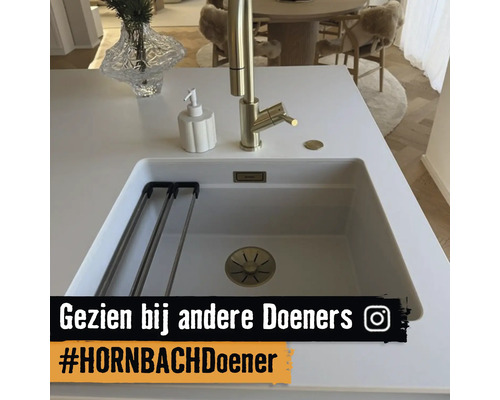 Moderne witte onderbouw spoelbak met gouden kraan, zeepdispenser en afdruiprek in een lichte keuken.