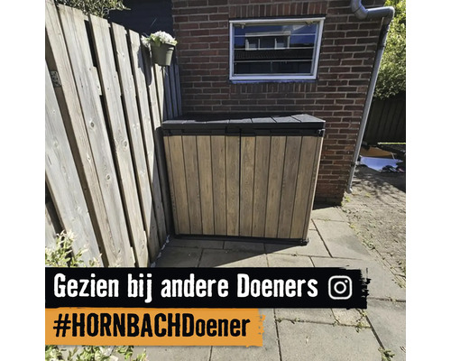 Tuinkast met houtlook op een betegeld terras voor een bakstenen muur en een houten schutting.