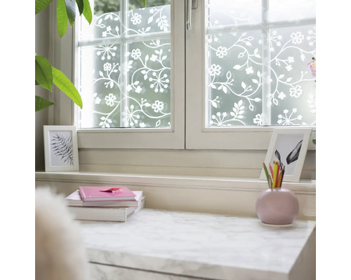 Raamfolie met bloemen- en rankenpatroon in wit op een matte ondergrond, decoratieve privacyfolie in een lichte kamer.