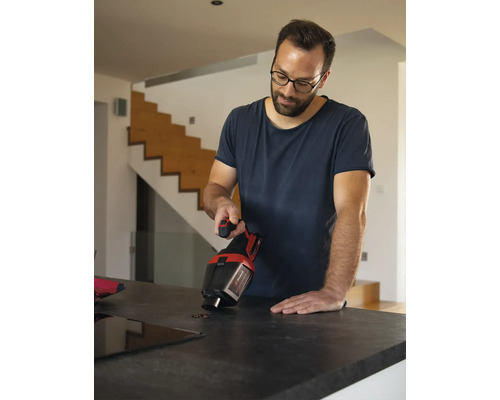 Een man gebruikt een Einhell kruimeldief om koffiebonen op te zuigen van een aanrecht in een lichte, moderne woning.