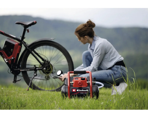 Een vrouw pompt de achterband van een fiets op met een Einhell accu-compressor op een grasveld.