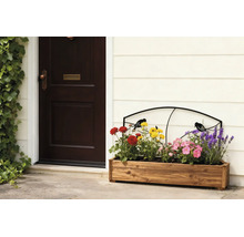 Houten plantenbak met kleurrijke bloemen en een zwart metalen klimrek met vogelmotief naast een donkere voordeur.