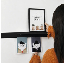 Iemand decoreert een zwarte wandplank met een fotolijst en twee kattenkaarten aan een witte muur.