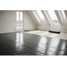 Zwarte dampremmende folie wordt gelegd op de vloer van een lichte, ruime zolderkamer met dakramen tijdens een renovatie.