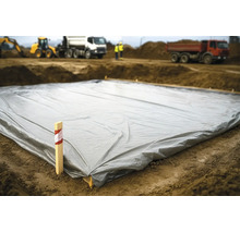 Grote grijze bouwfolie op de grond van een bouwplaats met graafmachines en vrachtwagens op de achtergrond.