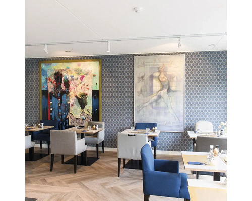 Restaurant met honingraat behang, visgraat parketvloer, gestoffeerde stoelen en twee grote moderne schilderijen aan de wand.
