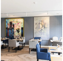 Restaurant met honingraat behang, visgraat parketvloer, gestoffeerde stoelen en twee grote moderne schilderijen aan de wand.