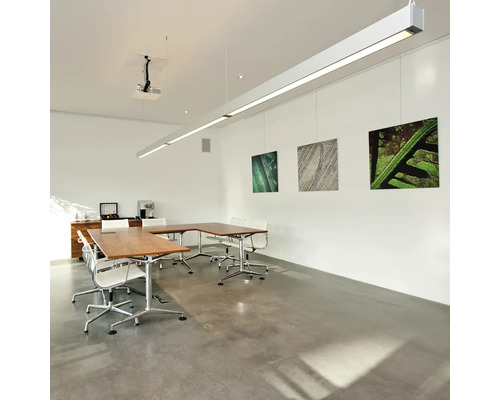 Moderne, lichte vergaderruimte met een U-vormige houten tafel, witte draaistoelen en een lange, hangende LED-lamp aan het witte plafond.