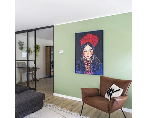 Woonkamer met groene muur, ingelijst schilderij van een vrouw, bruine lederen fauteuil en zwarte glazen deur naar de aangrenzende kamer.
