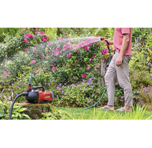 Einhell accu tuinpomp Aquinna bij het besproeien van de tuin met een tuinslang en een spuitpistool in een beplante tuin.