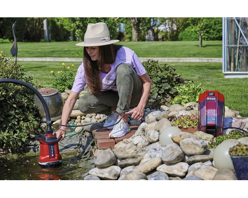 Vrouw bedient een Einhell accu-schoonwaterpomp bij een lichte tuinvijver met stenen en planten.