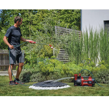 Een man besproeit de tuin met een accutuinpomp van Einhell die water uit een regenput pompt.