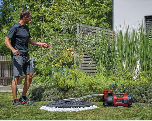 Een man besproeit de tuin met een accutuinpomp van Einhell die water uit een regenput pompt.