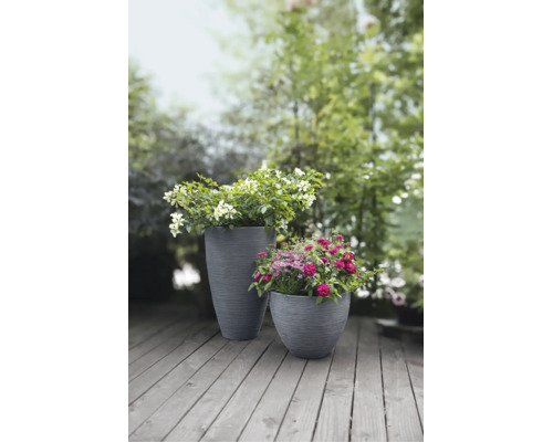 Twee grijze, geribbelde plantenbakken met bloeiende bloemen op een houten terras in de tuin.