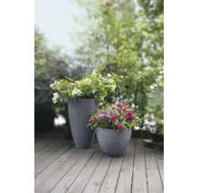 Twee grijze plantenbakken met rillenstructuur, gevuld met bloemen op een houten terras in de tuin.