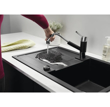 Een moderne zwarte keukenspoelbak met uittrekbare keukenkraan, waarbij een hand water over het afdruipgedeelte laat stromen.