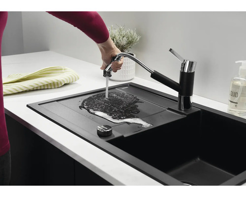 Een moderne zwarte keukenspoelbak met uittrekbare keukenkraan, waarbij een hand water over het afdruipgedeelte laat stromen.