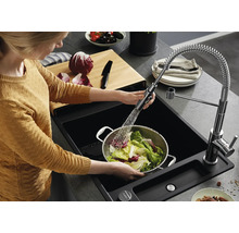 Persoon wast sla in een metalen vergiet in een zwarte inbouwspoelbak met uittrekbare keukenkraan en spiraalveer in een moderne keuken.