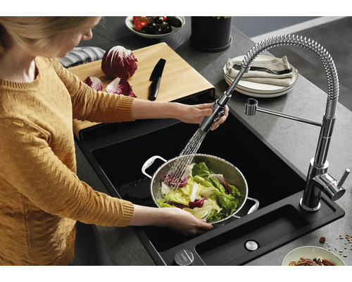 Persoon wast sla in een metalen vergiet in een zwarte inbouwspoelbak met uittrekbare keukenkraan en spiraalveer in een moderne keuken.